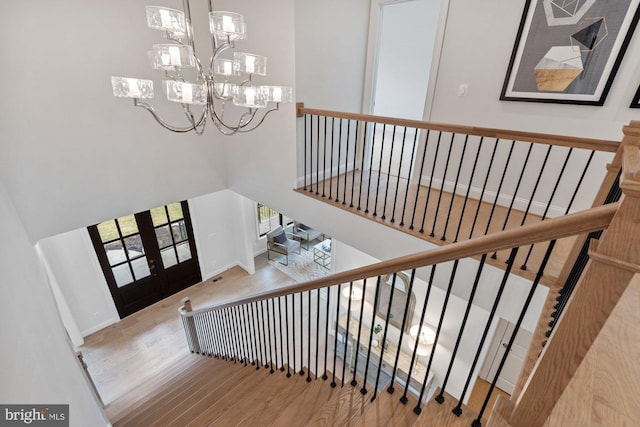 stairs with french doors, a high ceiling, an inviting chandelier, and wood finished floors