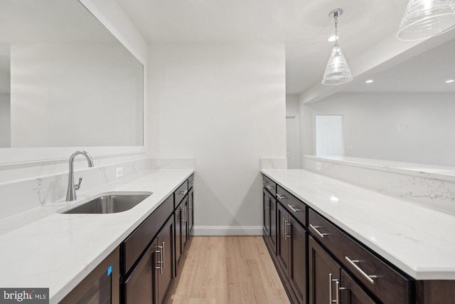 kitchen featuring dark brown cabinets, light wood-type flooring, light stone counters, a peninsula, and a sink