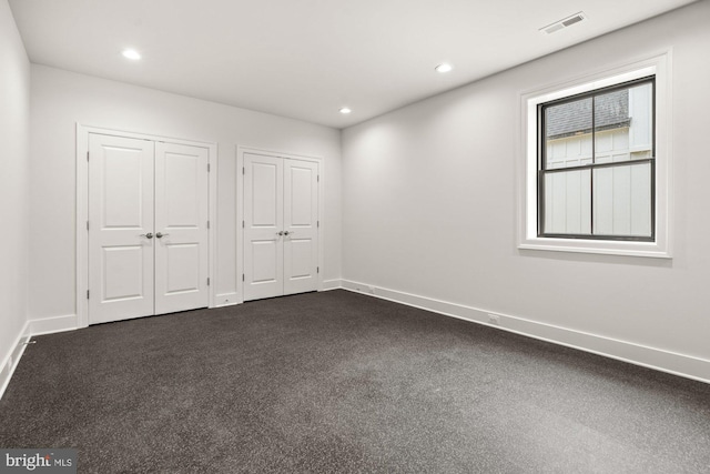 unfurnished bedroom featuring visible vents, two closets, baseboards, dark carpet, and recessed lighting