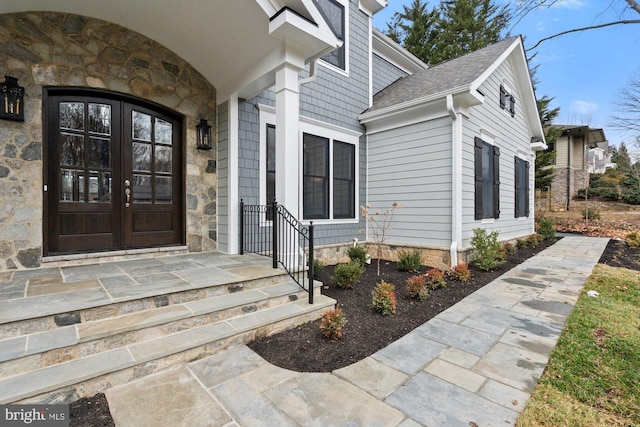 doorway to property featuring french doors, stone siding, and a shingled roof