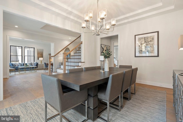 dining room featuring baseboards, stairway, a tray ceiling, an inviting chandelier, and wood finished floors