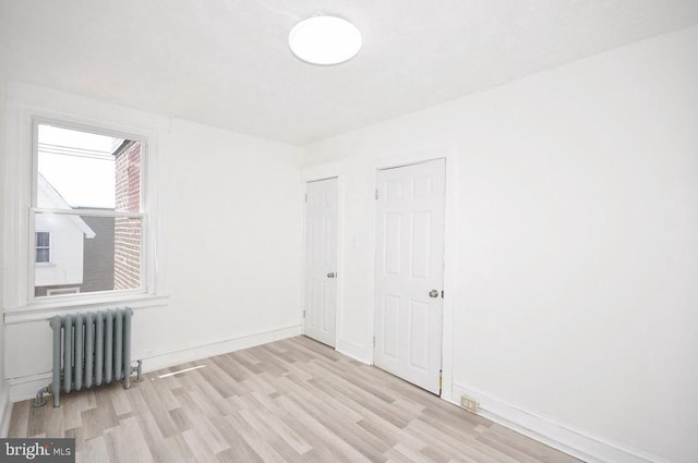 empty room with radiator, light wood-type flooring, and baseboards