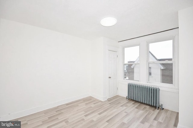 unfurnished room with radiator, baseboards, and light wood-style floors