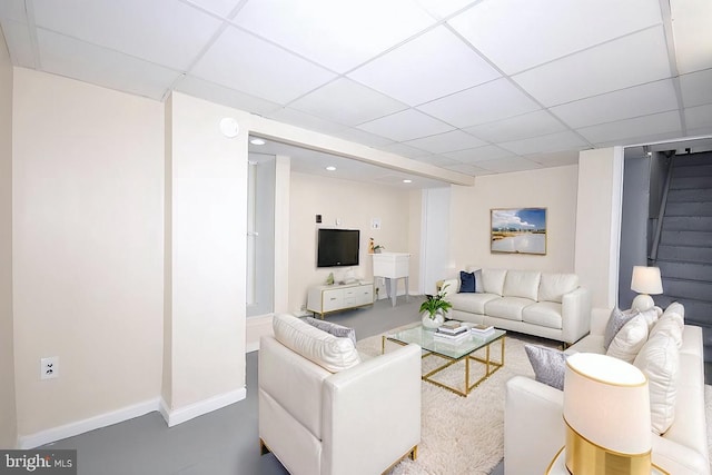 living area featuring stairs, a paneled ceiling, and baseboards