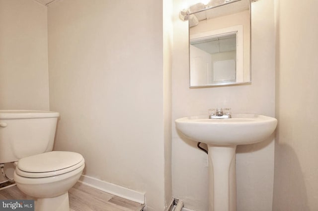 half bath featuring toilet, wood finished floors, and baseboards