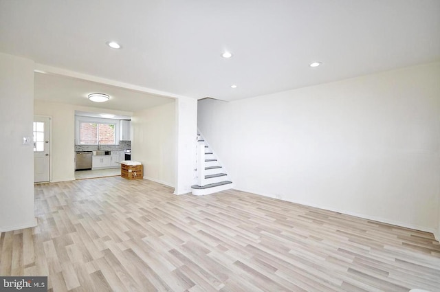 unfurnished living room featuring recessed lighting, stairway, a sink, and light wood finished floors