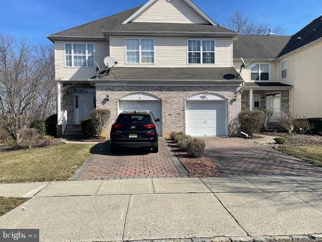 view of front of home with decorative driveway, brick siding, an attached garage, and a shingled roof