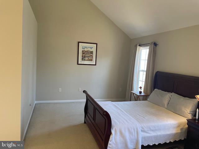 bedroom featuring lofted ceiling, light colored carpet, and baseboards