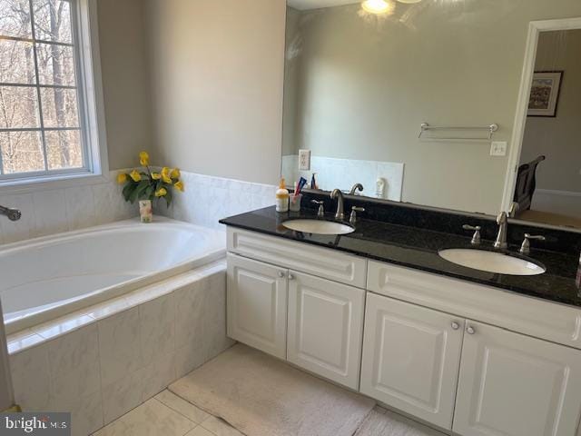 bathroom with tile patterned flooring, a garden tub, double vanity, and a sink