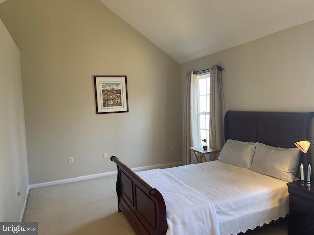 bedroom featuring baseboards, light carpet, and vaulted ceiling