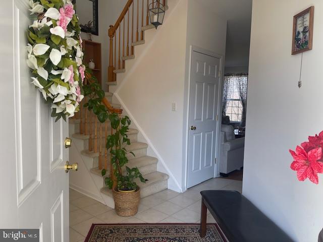 foyer entrance featuring light tile patterned floors, stairs, and baseboards