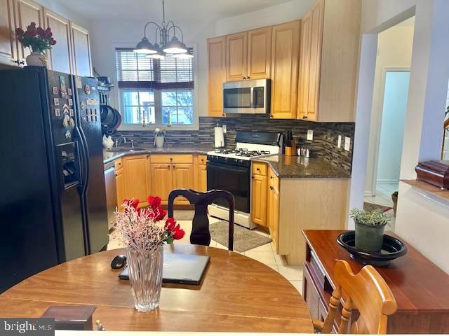 kitchen with dark countertops, tasteful backsplash, appliances with stainless steel finishes, an inviting chandelier, and light tile patterned floors