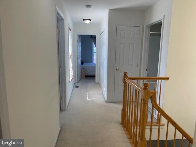 hallway featuring an upstairs landing, light carpet, and baseboards