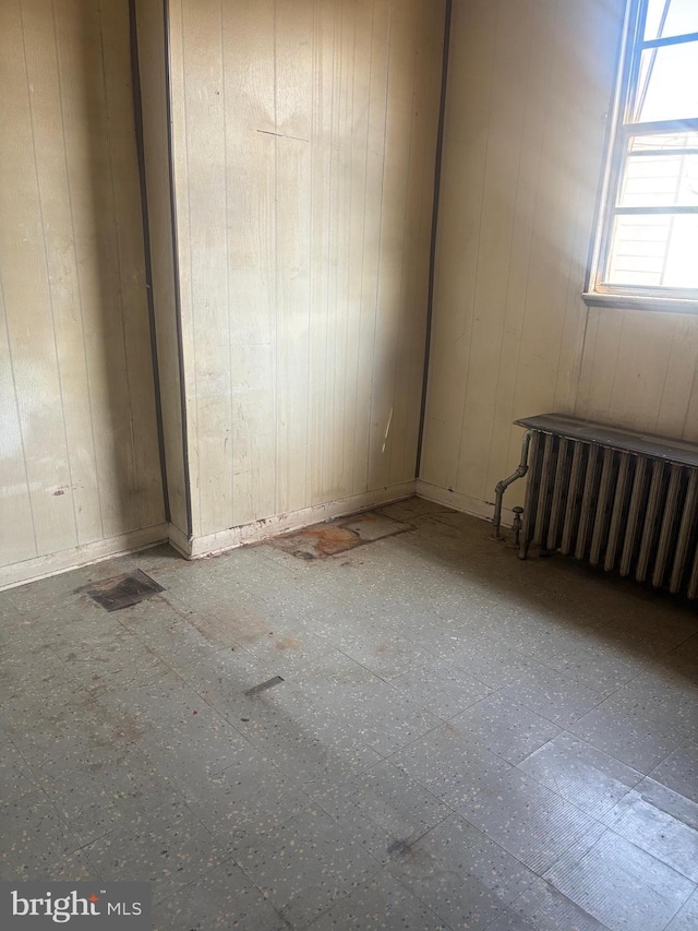 unfurnished room featuring tile patterned floors, wood walls, and radiator heating unit