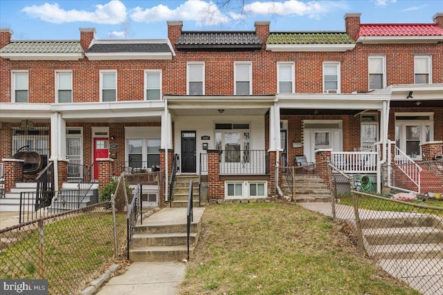 view of property featuring a tiled roof, brick siding, a porch, and fence