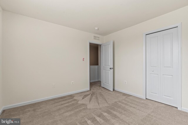 unfurnished bedroom featuring light colored carpet, visible vents, a closet, and baseboards