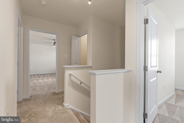 hall with baseboards, light colored carpet, and an upstairs landing