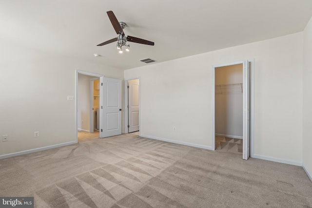 unfurnished bedroom featuring a walk in closet, baseboards, light colored carpet, and visible vents