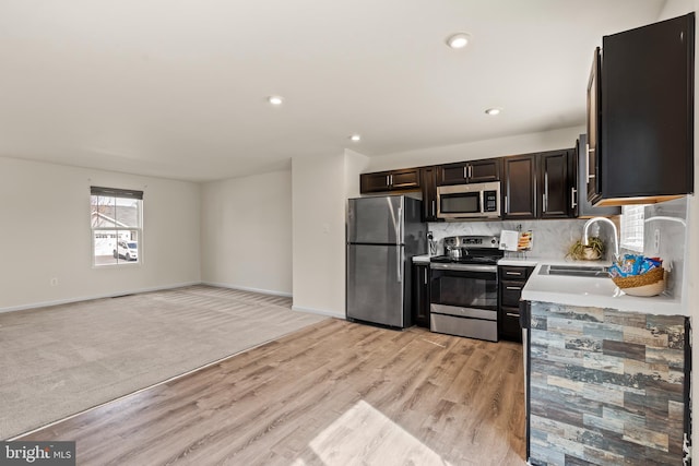 kitchen with light wood-style flooring, a sink, backsplash, appliances with stainless steel finishes, and light countertops