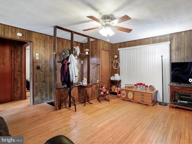 interior space featuring wood-type flooring, wooden walls, and a ceiling fan