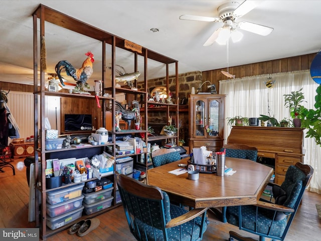 dining area featuring a ceiling fan, wood finished floors, and wood walls