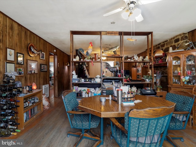 dining room featuring radiator, wooden walls, wood finished floors, and a ceiling fan