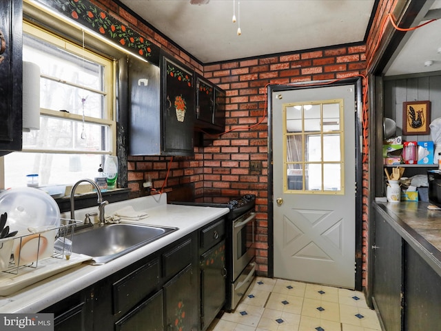 kitchen with a sink, dark cabinetry, brick wall, and stainless steel gas range