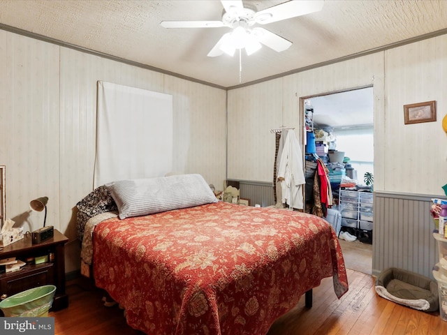 bedroom with a walk in closet, a ceiling fan, a textured ceiling, wood-type flooring, and crown molding