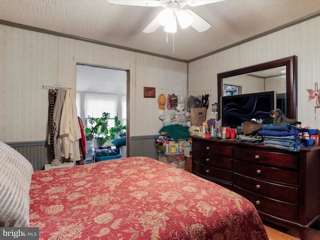 bedroom featuring a textured ceiling, ornamental molding, a ceiling fan, and wallpapered walls