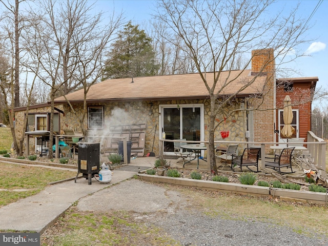 rear view of house featuring a patio, stone siding, and a chimney