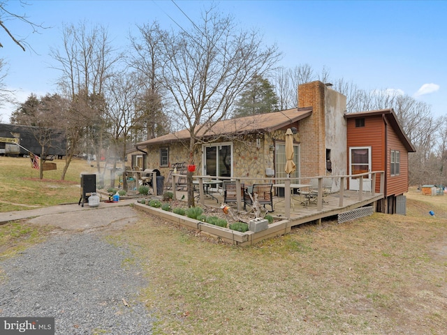 view of front facade with a deck, a chimney, a front yard, and stone siding