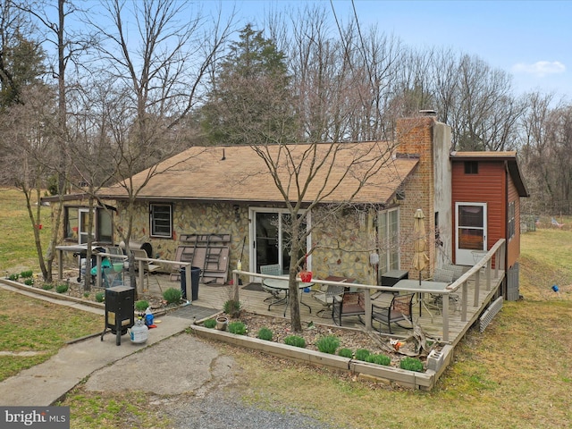 view of front of home with a front lawn, a wooden deck, stone siding, and a chimney