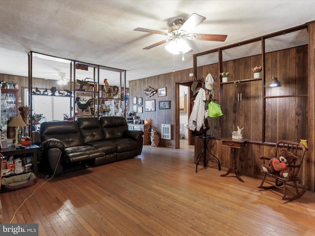 living area featuring heating unit, wood walls, wood-type flooring, and ceiling fan