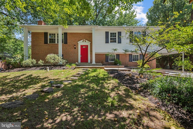 split foyer home with brick siding, a chimney, and a front yard