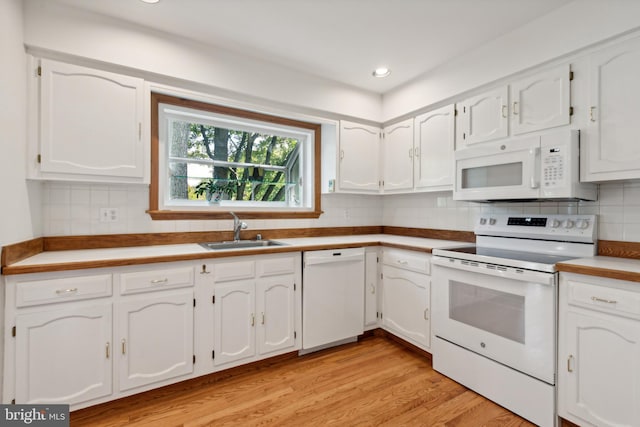 kitchen with white appliances, light wood finished floors, a sink, white cabinetry, and tasteful backsplash