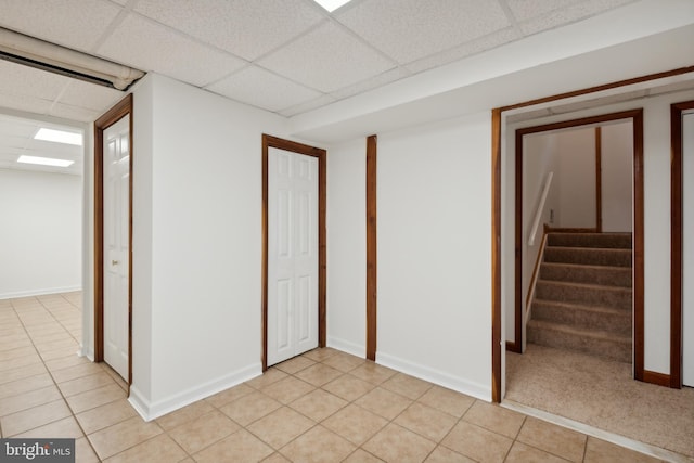 finished basement with light tile patterned floors, stairway, a paneled ceiling, and baseboards