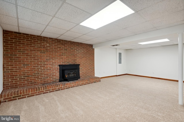 unfurnished living room with carpet flooring, baseboards, a wood stove, and a paneled ceiling