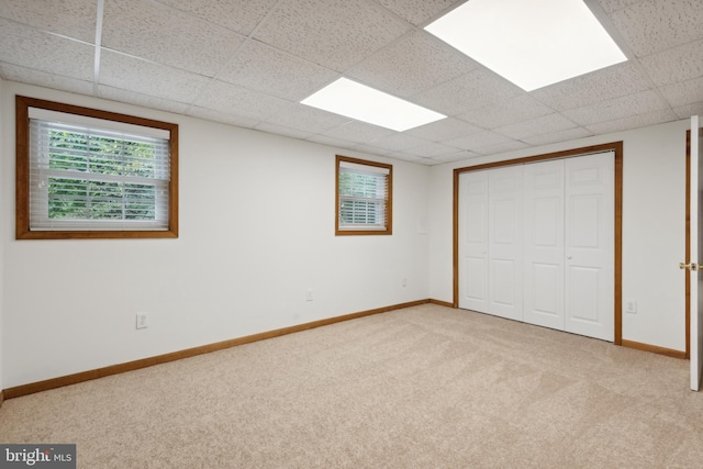 unfurnished bedroom with a paneled ceiling, baseboards, a closet, and light carpet