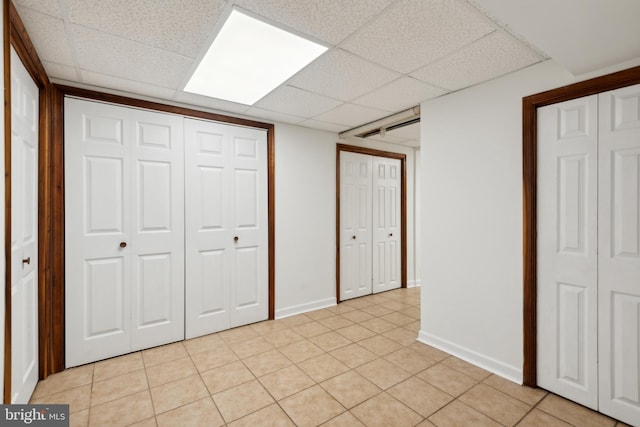 unfurnished bedroom with light tile patterned floors, a drop ceiling, and baseboards