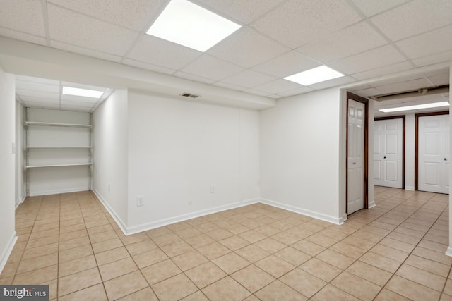 finished below grade area featuring light tile patterned floors, a paneled ceiling, and baseboards