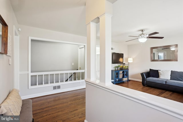 living area with visible vents, baseboards, ceiling fan, dark wood-style flooring, and ornate columns