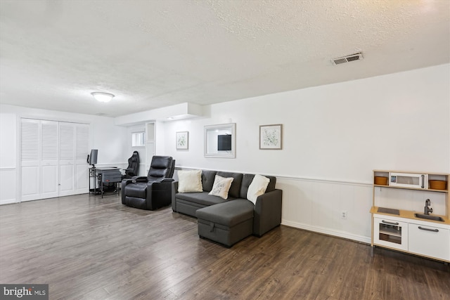 living room featuring visible vents, dark wood-type flooring, wainscoting, and a textured ceiling