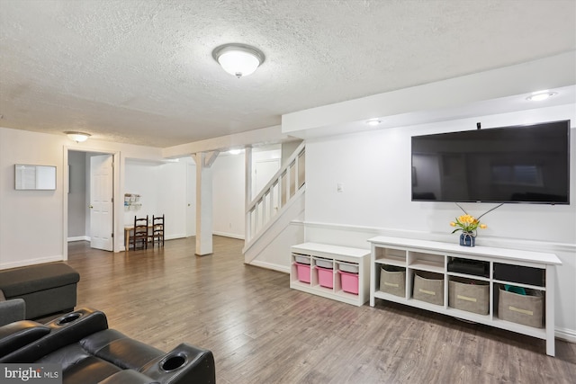 living area with baseboards, a textured ceiling, wood finished floors, and stairs