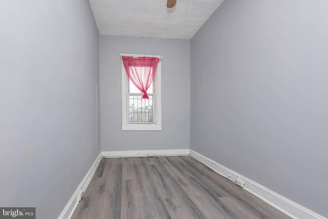 empty room with a textured ceiling, baseboards, and wood finished floors