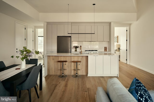 kitchen with modern cabinets, a breakfast bar, freestanding refrigerator, light wood finished floors, and light countertops