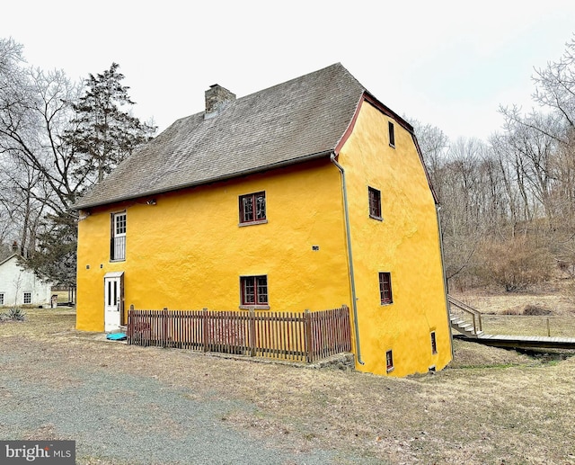 view of side of home featuring stucco siding, a chimney, and fence