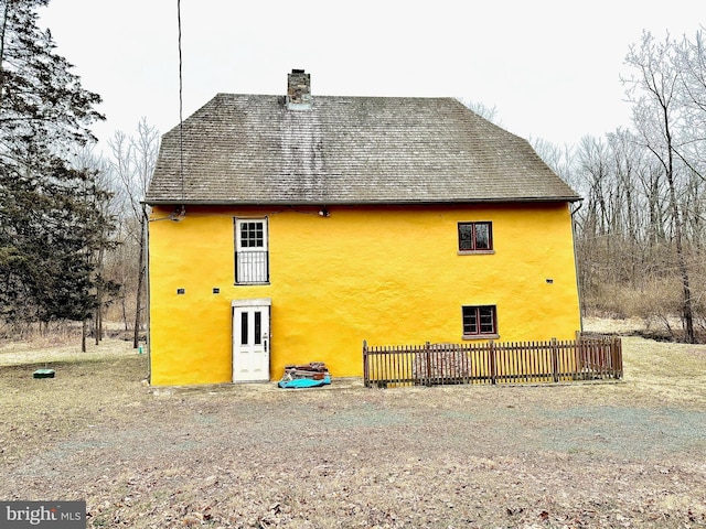 rear view of property with a shingled roof, stucco siding, a chimney, and fence