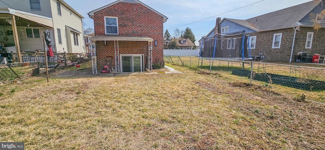 rear view of house with a trampoline, brick siding, a yard, and a fenced backyard