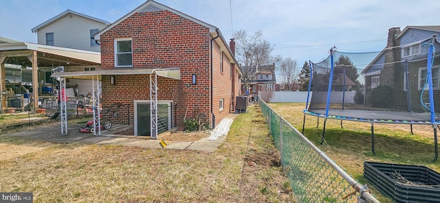 view of side of property featuring a fenced backyard, central AC, a trampoline, a lawn, and brick siding