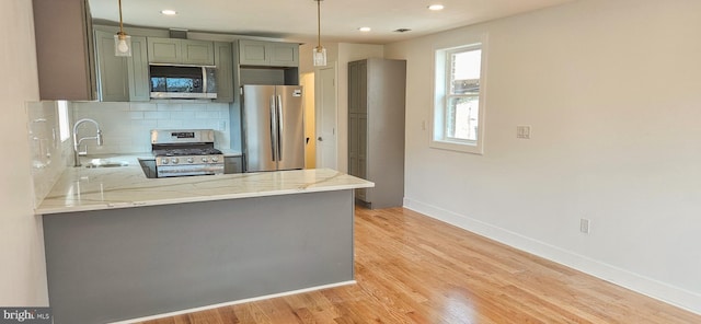 kitchen with a sink, light wood-style floors, appliances with stainless steel finishes, a peninsula, and decorative backsplash